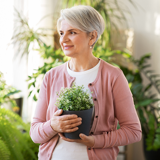 happy senior woman with flower in pot at home